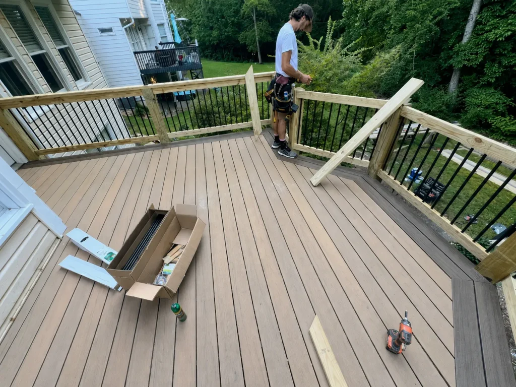 Worker fitting a deck railing with wooden posts and black balusters, with tools on the tan decking.
