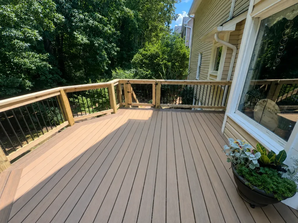 Tan backyard deck with wooden railing posts, black balusters, and a planter beside the sliding glass door.