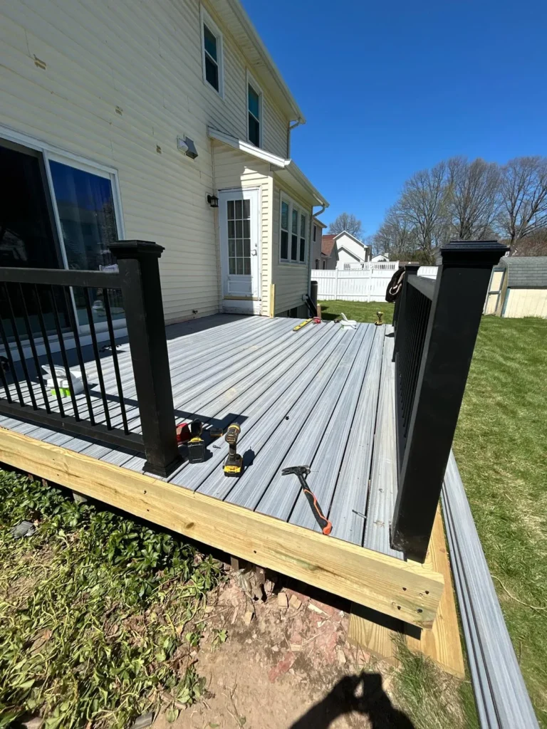 Gray deck under construction with black railing posts, exposed perimeter framing, and tools on the boards.