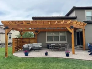 Wooden pergola covering a curved paver patio with a dining table, outdoor sofa, and horizontal privacy screen.