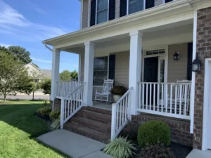 Covered front porch with white columns, white railings, rocking chairs, and brick entrance steps.