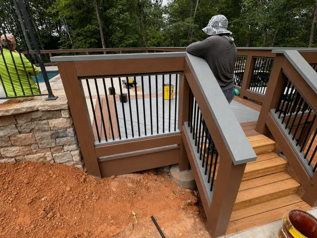 Workers beside deck stairs with brown railing frames, gray handrails, and black balusters.