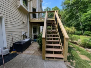 Straight outdoor staircase with wooden handrails and black balusters leading to an elevated backyard deck.
