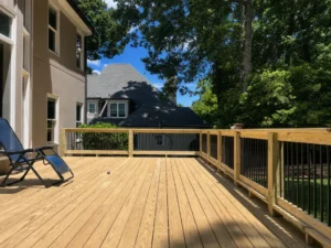 Sunlit wooden deck with matching railing posts, black balusters, and a reclining chair beside the house.